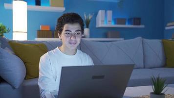 contento joven Adolescente chico trabajando en ordenador portátil a noche a hogar. chico mecanografía texto utilizando teclado ordenador portátil a mesa. enviar mensajes de texto, Adolescente chico, hallazgo un novia. video