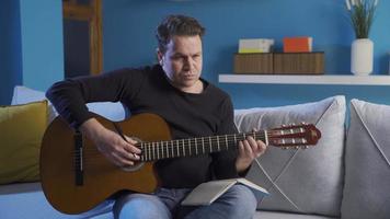 talentoso hombre quien compone música y escribe canciones creativo adulto hombre jugando guitarra melodía y tomando notas en cuaderno. inspiración, maestro video