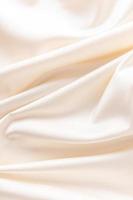 luxurious wedding satin background with delicate folds. elegant satin fabric of beige color, ivory. vertical view. photo