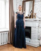 A woman in a blue dress stands in front of a fireplace photo