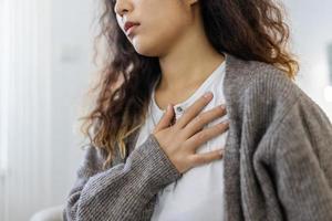 estresado joven mujer sensación dolor y conmovedor cofre sufrir desde angustia enfermedad a hogar mientras teniendo corazón ataque, infarto foto