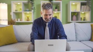 Delightful and happy mature businessman working from home on laptop. Relaxing mature businessman sitting alone on sofa at home working on laptop, doing business, following stock market. video