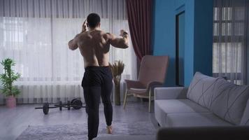 joven atleta haciendo kickboxing en contra el aire a hogar con su espalda transformado. muscular deportista boxeo de sombra a hogar con su espalda convertido a el cámara, pateando y puñetazos. video