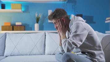 nerveus en benadrukt jong Mens Bij huis alleen attent en ongelukkig. depressief jong Mens zittend Aan sofa laat Bij nacht denken nerveus en bezorgd. video