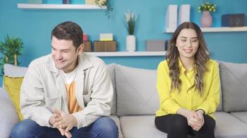 First date. Shy, young attractive lovers looking at each other, excited and happy. Happy and excited couple sitting on sofa at home, first date excitement and shyness. video