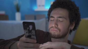 depresso giovane uomo guardare a il suo inteligente mobile Telefono perdente motivazione. giovane uomo guardare a il suo smartphone a casa annoiato con cattivo notizia, sensazione depresso, indifeso e senza speranza video