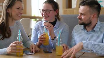 Three friends sit in a cafe, drink juice and have fun communicating video