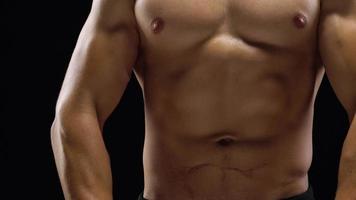 hombre muestra un muscular fuerte cuerpo de cerca en un negro antecedentes. abdominal músculos tiempo video