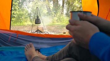 Woman is drinking tea in a tent and looking at the fire in front of her video