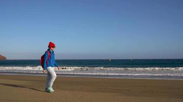 ativo caminhante mulher anda em em a de praia para a água. caucasiano jovem mulher com mochila em tenerife, canário ilhas video