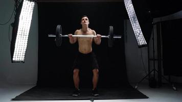 Man is doing exercises with a barbell, training on a black background in the studio. Half body in frame video