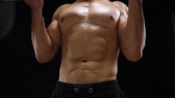 Man is doing exercises with a barbell, training on a black background in the studio. Half body in frame video