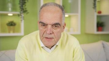 frustrato e scontroso vecchio uomo guardare a telecamera a casa. annoiato e scontroso pensionato vecchio uomo guardare a telecamera nel un arrabbiato umore. video