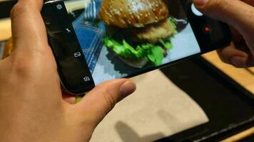 niña hace un foto de hamburguesa y tomate jugo en un teléfono inteligente en un café cerca arriba video