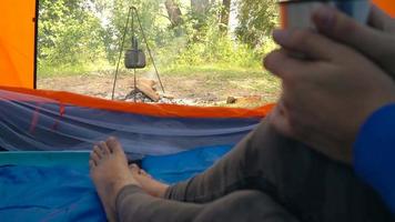 Woman is drinking tea in a tent and looking at the fire in front of her video