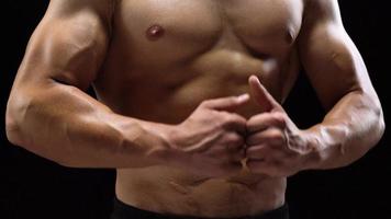 hombre muestra un muscular fuerte cuerpo de cerca en un negro antecedentes. abdominal músculos tiempo video