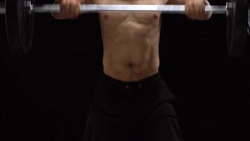 Man is doing exercises with a barbell, training on a black background in the studio. Half body in frame video