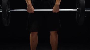 Man is doing exercises with a barbell, training on a black background in the studio. Half body in frame video