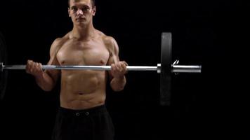 Man is doing exercises with a barbell, training on a black background in the studio. Half body in frame video