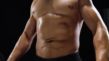Man shows a muscular strong body close-up on a black background. Abdominal muscles tense video