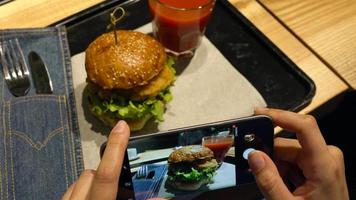 menina faz uma foto do hamburguer e tomate suco em uma Smartphone dentro uma cafeteria fechar acima video