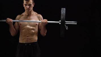 Man is doing exercises with a barbell, training on a black background in the studio. Half body in frame video