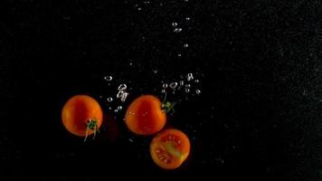 Red tomatoes fall and float in water, black background, slow motion video