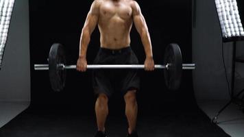 Man is doing exercises with a barbell, training on a black background in the studio. Half body in frame video