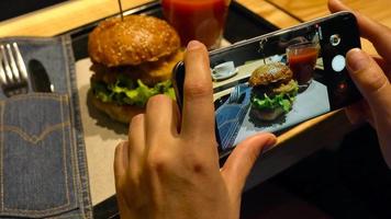 menina faz uma foto do hamburguer e tomate suco em uma Smartphone dentro uma cafeteria fechar acima video