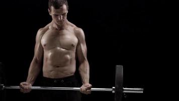 Man is doing exercises with a barbell, training on a black background in the studio video