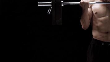 Man is doing exercises with a barbell, training on a black background in the studio video