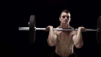 Man is doing exercises with a barbell, training on a black background in the studio video