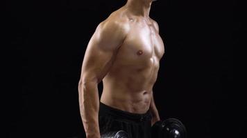 Man is doing exercises with a barbell, training on a black background in the studio. Half body in frame video