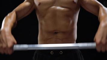 Man is doing exercises with a barbell, training on a black background in the studio. Half body in frame video