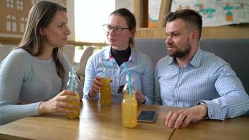 Tres amigos sentar en un cafetería, bebida jugo y tener divertido comunicado video