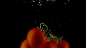 Red tomatoes fall and float in water, black background, slow motion video