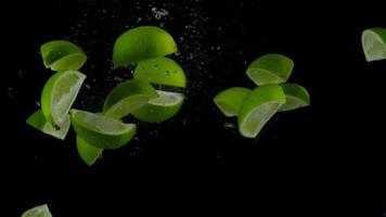 Lime pieces fall and float in water, black background. Slow motion video