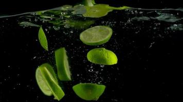 citron vert pièces tomber et flotte dans eau, noir Contexte. lent mouvement video