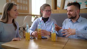 Three friends sit in a cafe, drink juice and have fun communicating video