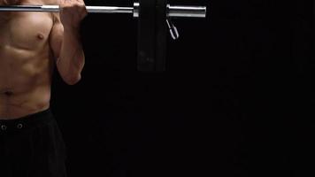 Man is doing exercises with a barbell, training on a black background in the studio. Half body in frame video