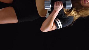 Woman is doing exercises with a barbell, training on a black background in the studio. Half body in frame video