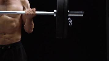 hombre es haciendo ejercicios con un barra con pesas, formación en un negro antecedentes en el estudio. medio cuerpo en marco video