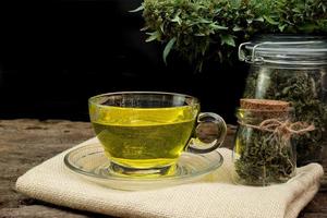 Cannabis tea in a clear glass cup with a marijuana bud in a jar on a wooden and the black background photo