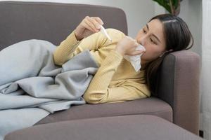 joven asiático mujer teniendo alto fiebre mientras comprobación cuerpo temperatura, hembra estornudos y líquido nariz con estacional influenza, alérgico, digital termómetro, virus, coronavirus, enfermedad, respiratorio foto