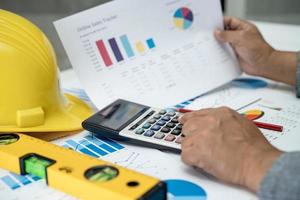 Asian engineer with architectural house plan project blueprint, graph and yellow helmet and engineering construction tools. photo