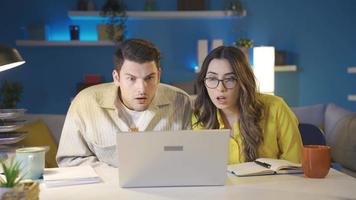 a casado casal concentrando em a computador portátil tela estão chocado de o que elas ver. video
