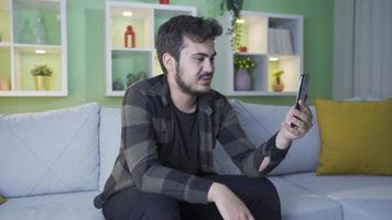 roligt ung man chattar med hans vänner på facetime. Lycklig och rolig man video chattar med hans vänner på hans smartphone på Hem.