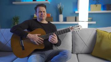 emotional und traurig Erwachsene Mann Leiden von Schmerzen und Einsamkeit beim heim. Zuhause allein, deprimiert, traurig und Weinen, Sitzung auf das Sofa mit seine Gitarre. video