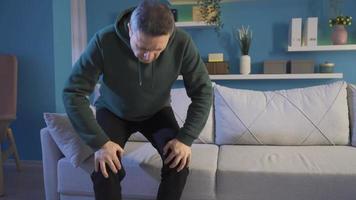 maturo uomo con acuto reumatismo sfregamento il suo ginocchia. uomo sofferenza acuto ginocchio dolore a casa, reumatismi, comune dolori. video