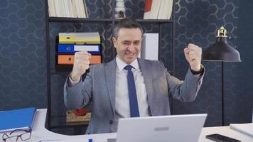 The fun and lively businessman rejoices at the good news he receives at the office. Man working on laptop in office, rejoicing at the good news he receives, achieves his goals. video